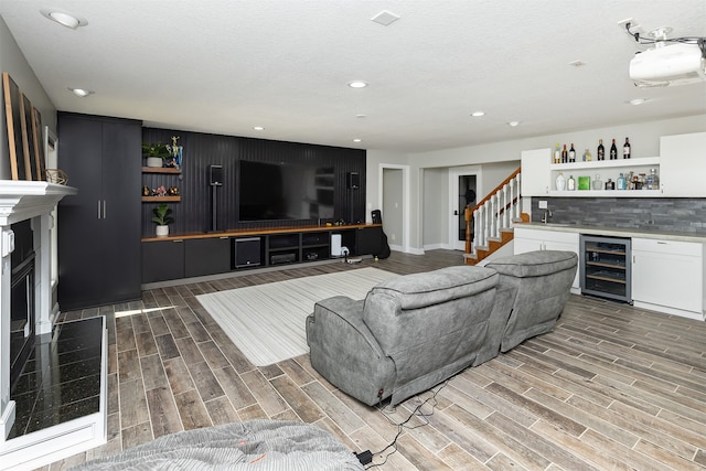 living area featuring beverage cooler, stairway, wood finish floors, a bar, and a fireplace