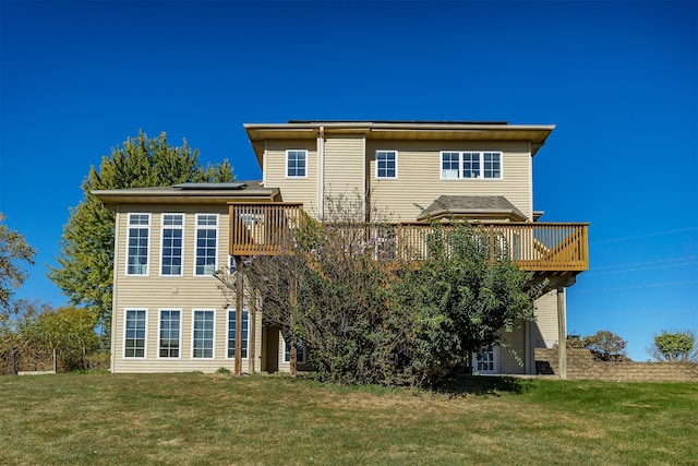 rear view of property featuring a deck, a yard, and roof mounted solar panels