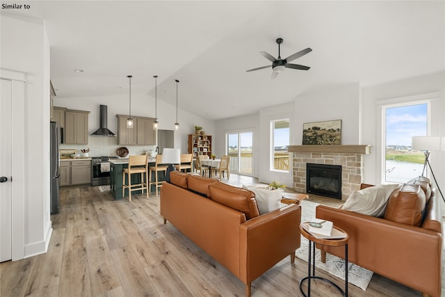 living room with vaulted ceiling, a fireplace, light hardwood / wood-style floors, and ceiling fan