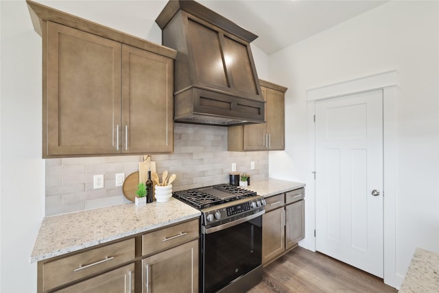 kitchen featuring premium range hood, decorative backsplash, light stone counters, dark hardwood / wood-style flooring, and stainless steel range with gas stovetop