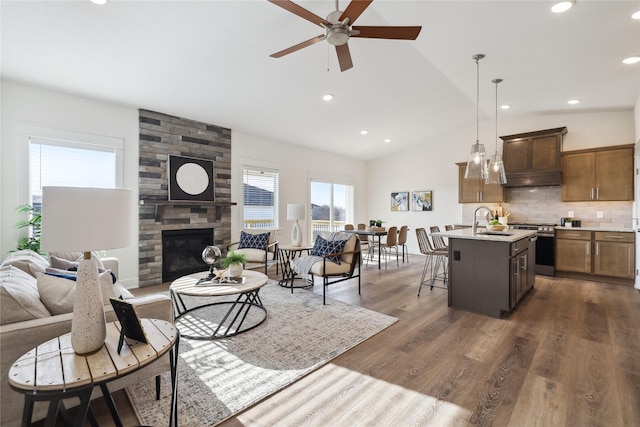 living room with ceiling fan, a large fireplace, sink, dark hardwood / wood-style flooring, and vaulted ceiling