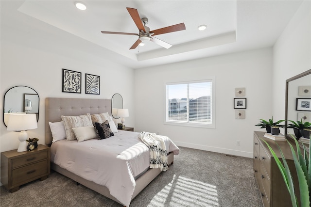 carpeted bedroom featuring a tray ceiling and ceiling fan