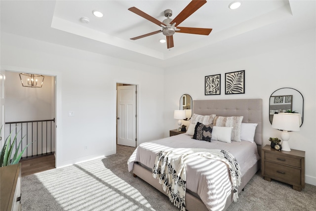 carpeted bedroom with a tray ceiling and ceiling fan with notable chandelier