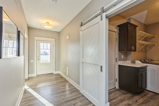 entryway featuring a barn door, washer / dryer, a textured ceiling, and light hardwood / wood-style flooring