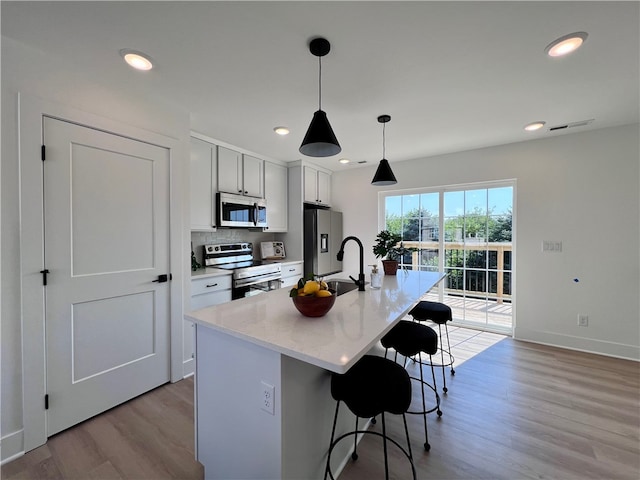 kitchen with stainless steel appliances, a center island with sink, a breakfast bar, pendant lighting, and light wood-type flooring