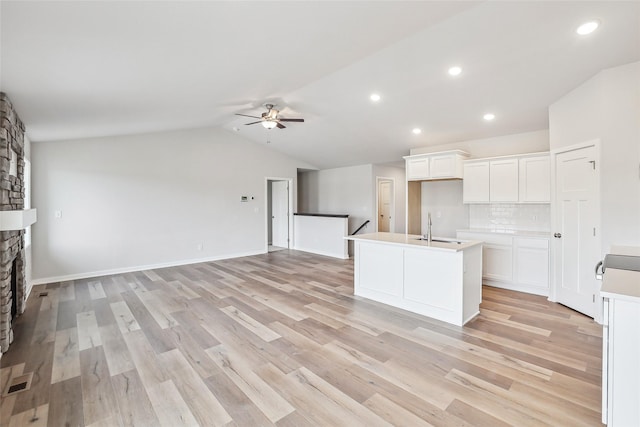 kitchen featuring a center island with sink, a fireplace, white cabinetry, lofted ceiling, and tasteful backsplash