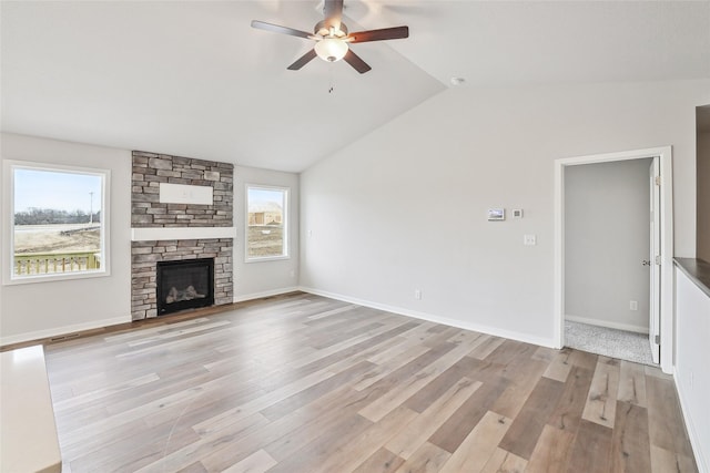 unfurnished living room with light hardwood / wood-style floors, ceiling fan, vaulted ceiling, and a stone fireplace