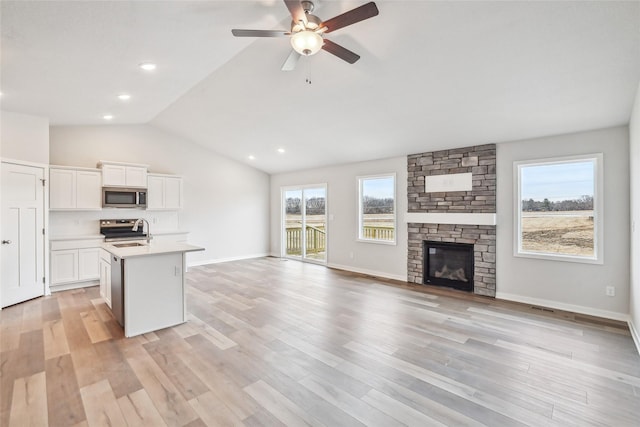 kitchen with stainless steel appliances, white cabinetry, light hardwood / wood-style floors, a kitchen island with sink, and a stone fireplace