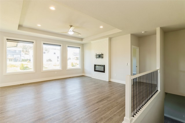 unfurnished living room featuring a raised ceiling, wood-type flooring, a large fireplace, and ceiling fan