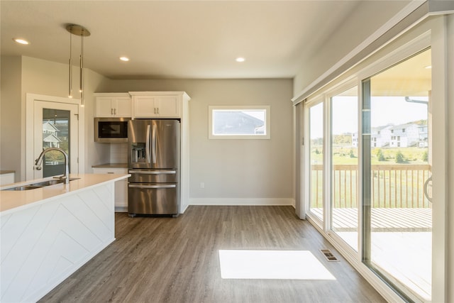 kitchen with hanging light fixtures, stainless steel appliances, a wealth of natural light, sink, and white cabinets