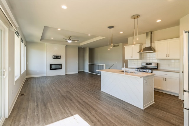 kitchen featuring wall chimney exhaust hood, a center island with sink, decorative light fixtures, gas stove, and dark hardwood / wood-style flooring