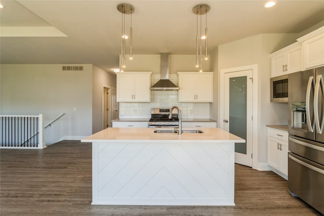 kitchen featuring stainless steel appliances, wall chimney exhaust hood, pendant lighting, and a kitchen island with sink