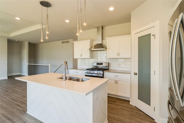 kitchen featuring wall chimney range hood, stainless steel appliances, a center island with sink, sink, and white cabinetry