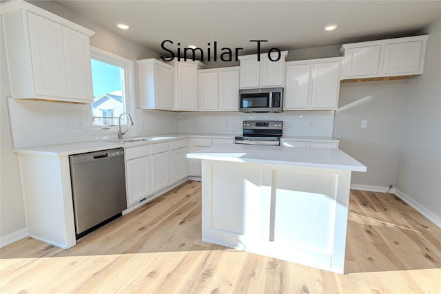 kitchen featuring light countertops, appliances with stainless steel finishes, white cabinets, a kitchen island, and a sink