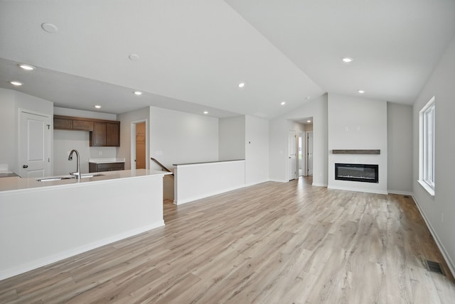unfurnished living room with light wood finished floors, recessed lighting, a sink, visible vents, and vaulted ceiling