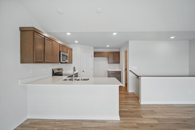 kitchen featuring stainless steel appliances, a peninsula, light countertops, and a sink