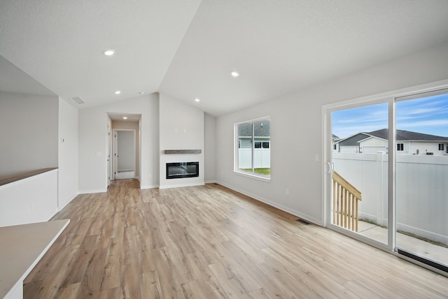 unfurnished living room featuring a glass covered fireplace, visible vents, vaulted ceiling, light wood-style flooring, and baseboards