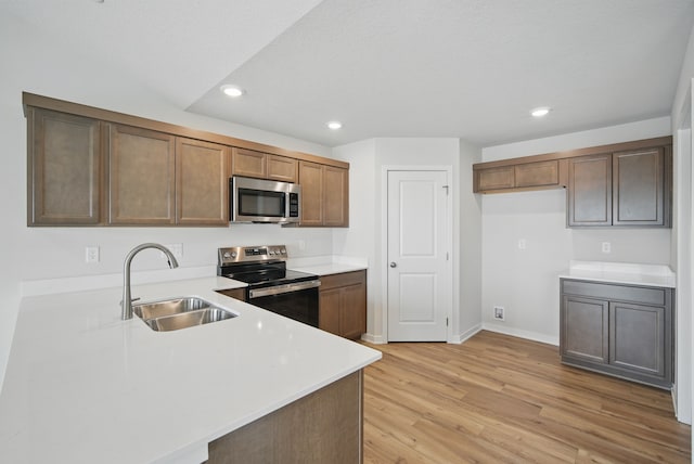 kitchen featuring recessed lighting, stainless steel appliances, light countertops, light wood finished floors, and a sink
