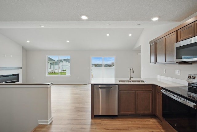 kitchen with a sink, stainless steel appliances, light wood-type flooring, vaulted ceiling, and a peninsula