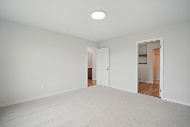 unfurnished bedroom featuring a spacious closet, carpet floors, and baseboards