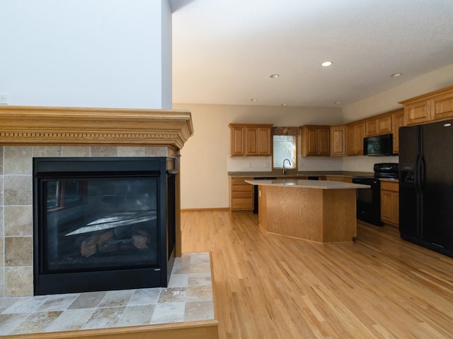 kitchen with light wood-type flooring, black appliances, a tile fireplace, sink, and a center island