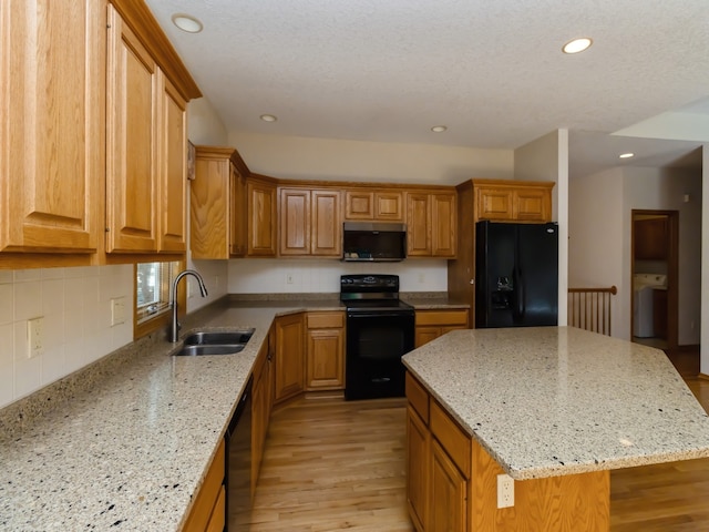 kitchen with a kitchen island, sink, black appliances, light wood-type flooring, and light stone counters