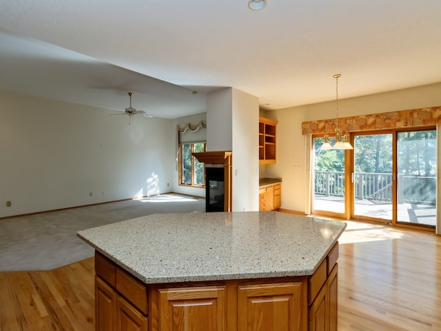 kitchen featuring a kitchen island, ceiling fan, pendant lighting, light stone counters, and light hardwood / wood-style flooring