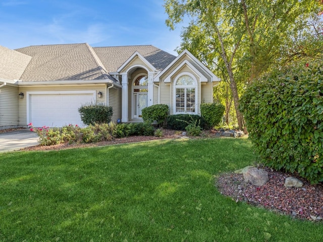 view of front of property featuring an attached garage, concrete driveway, a front lawn, and a shingled roof