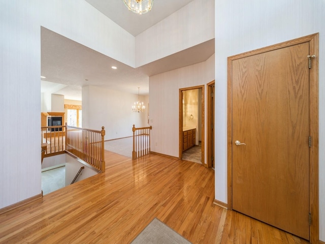 hallway featuring wood finished floors, an upstairs landing, baseboards, and a chandelier