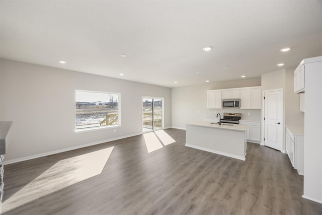 kitchen with appliances with stainless steel finishes, open floor plan, dark wood-style flooring, and an island with sink