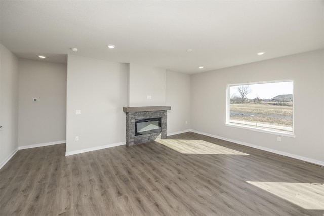 unfurnished living room featuring a stone fireplace, wood finished floors, and baseboards