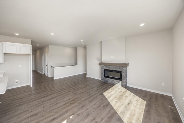 unfurnished living room featuring a stone fireplace, recessed lighting, dark wood-style floors, and baseboards