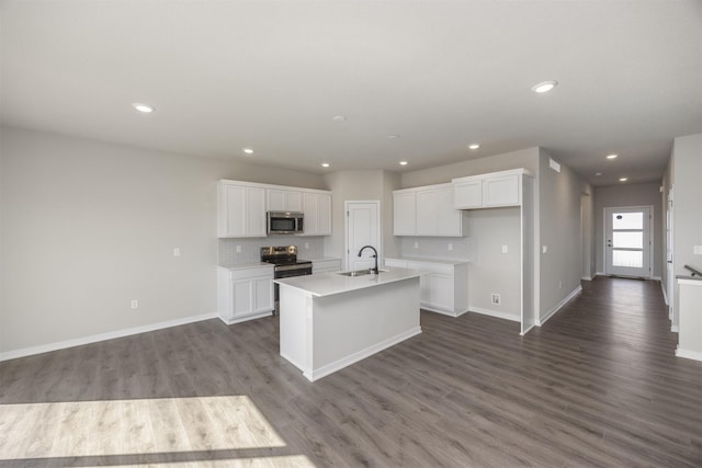 kitchen featuring dark wood-type flooring, a center island with sink, a sink, white cabinetry, and appliances with stainless steel finishes