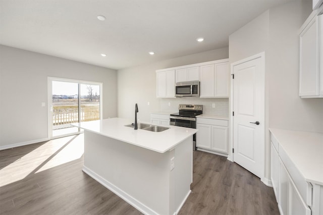 kitchen with dark wood-style flooring, stainless steel appliances, a sink, white cabinets, and backsplash