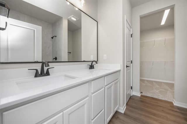 full bathroom featuring double vanity, a walk in closet, a shower, and a sink