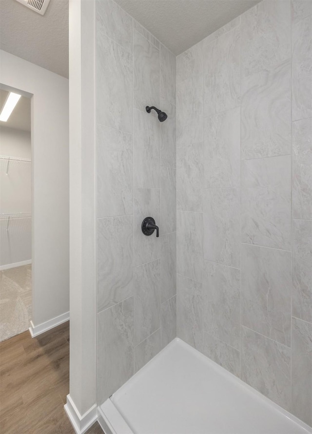 bathroom featuring a spacious closet, baseboards, tiled shower, wood finished floors, and a textured ceiling