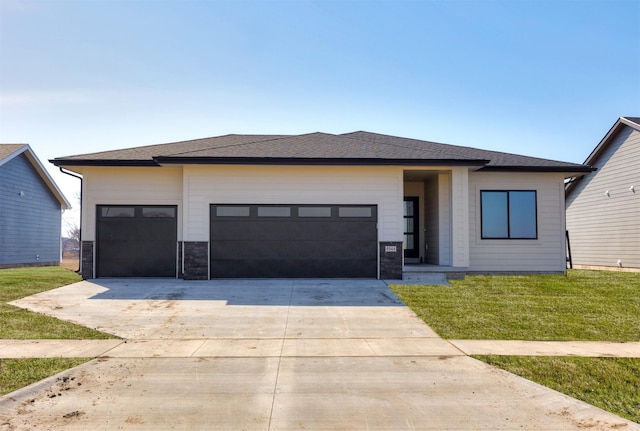 prairie-style house featuring an attached garage, concrete driveway, a front yard, and roof with shingles