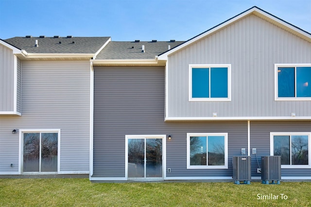 rear view of house featuring central AC unit and a lawn