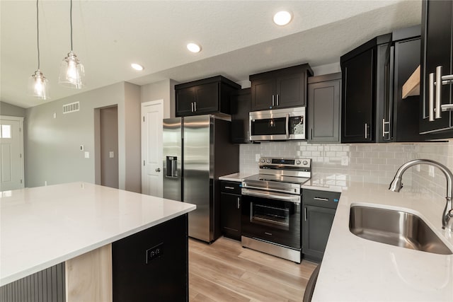 kitchen featuring decorative backsplash, hanging light fixtures, appliances with stainless steel finishes, light wood-type flooring, and sink