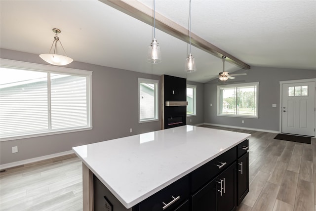 kitchen featuring vaulted ceiling with beams, a kitchen island, ceiling fan, pendant lighting, and light hardwood / wood-style flooring