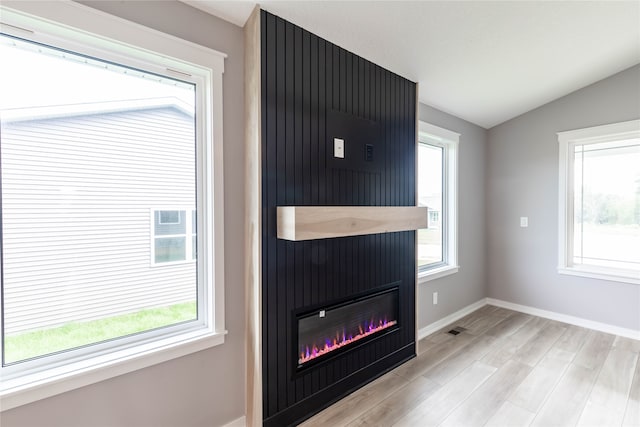 unfurnished living room with vaulted ceiling, a fireplace, and light hardwood / wood-style floors