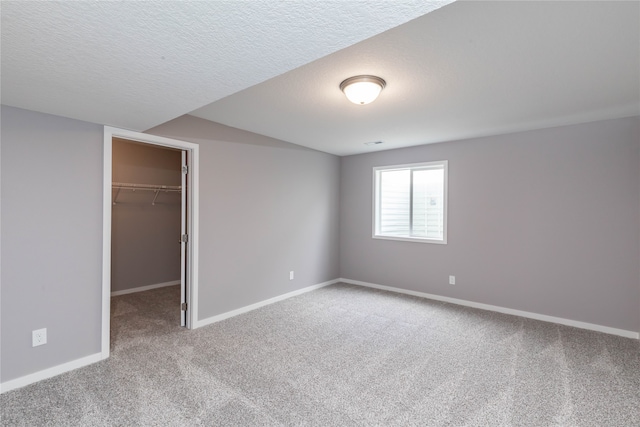 unfurnished bedroom featuring a spacious closet, a textured ceiling, carpet flooring, and a closet