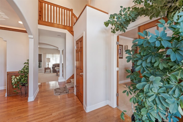 foyer entrance featuring light hardwood / wood-style flooring, crown molding, and decorative columns