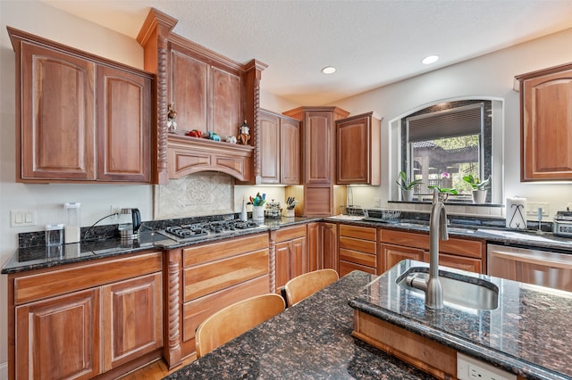 kitchen with a textured ceiling, stainless steel appliances, sink, and dark stone counters