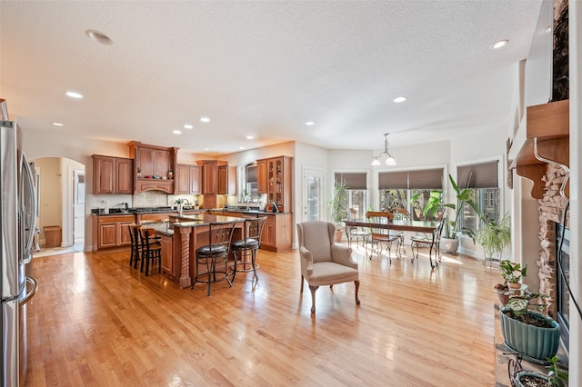 kitchen with an island with sink, a breakfast bar, stainless steel fridge, decorative light fixtures, and light hardwood / wood-style flooring