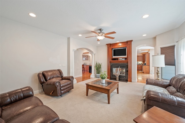 carpeted living room featuring a large fireplace, ornate columns, and ceiling fan