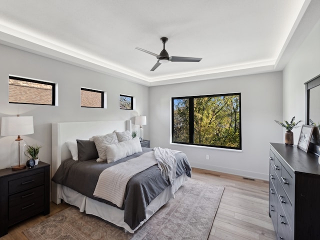 bedroom featuring ceiling fan, light wood-type flooring, and a tray ceiling