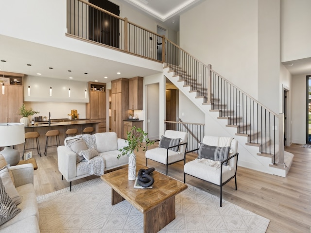 living room with a towering ceiling, sink, and light hardwood / wood-style flooring