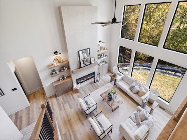 living room with ceiling fan, light hardwood / wood-style floors, and a towering ceiling