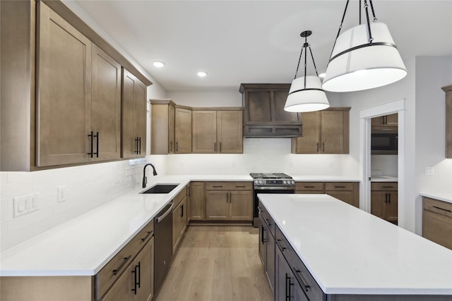 kitchen with stainless steel appliances, sink, pendant lighting, light hardwood / wood-style floors, and a kitchen island